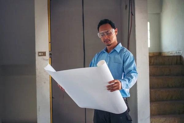 Architecture man engineer civil worker look at blueprint. Construction engineer man hold blueprint wear blue shirt safety white hard hat construction site. Industry labour worker real estate concept