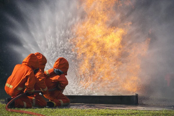 Firefighter Rescue team training in fire fighting extinguisher. Firefighter teamwork fighting with flame using fire hose chemical water foam spray engine. Fireman wear hard hat, safety suit uniform