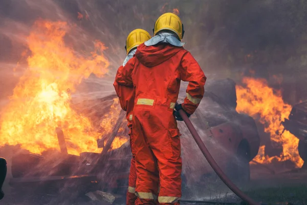 Firefighter Rescue training in fire fighting extinguisher. Firefighter fighting with flame using fire hose chemical water foam spray engine. Fireman wear hard hat, safety suit uniform for protection