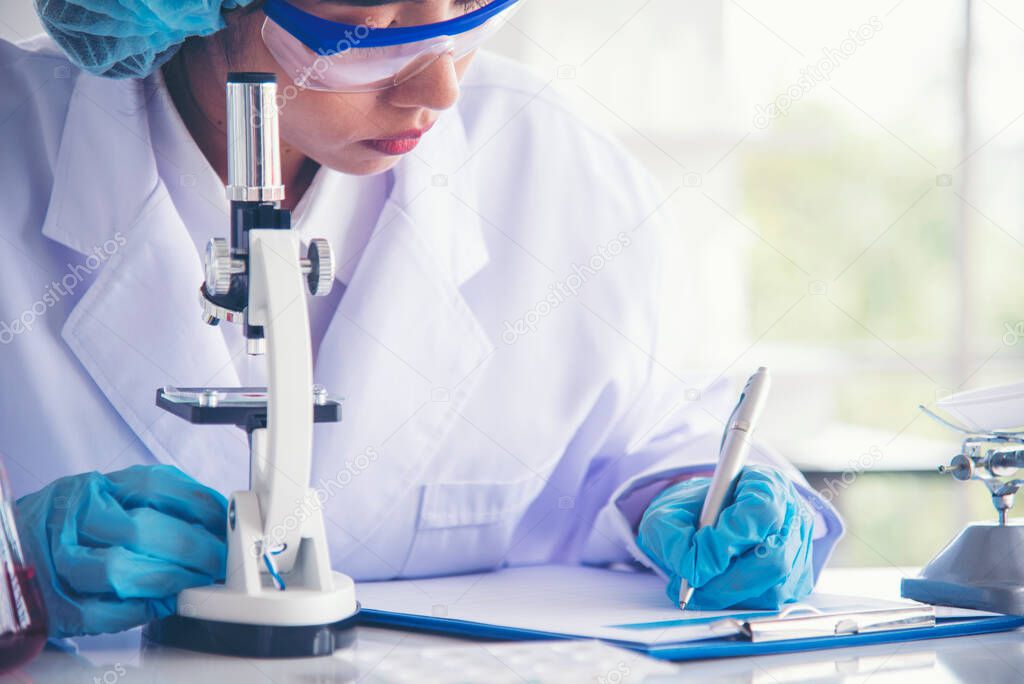 Researcher biology chemistry. Asian Female technician laboratory using microscope blood test. Asian Woman scientist hand write note research in medical lab look at science microscope medical test