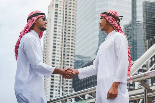 Arab Businessman Muslim dress shaking hands together in modern city UAE background. Muslim Men Teamwork business partner handshake with Partnership. diversity multiracial arab people trust commitment