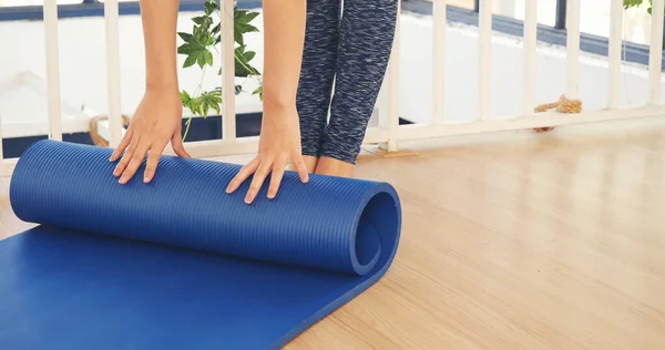 Woman hands rolled up yoga mat on gym floor in yoga fitness training room. Home workout woman close up hands rolling foam yoga gym mat. Woman barefoot home workout sportive healthy lifestyle concept