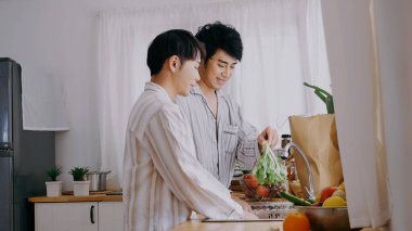 Asian people happy time smile, laugh in kitchen. Best friend LGBTQ lifestyle. Happy Asian gay couple homosexual cooking together in kitchen prepare fresh vegetable make organic salad healthy food.