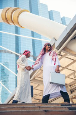 Arap iş adamı müslüman elbisesi modern şehir BAE arka planında el sıkışıyor. Müslüman Erkekler Takım Çalışması İş Ortağıyla Ortaklık tokalaşması. çok ırklı Arap halkı bağlılığa güvenir