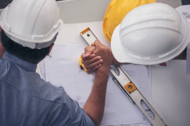 İnşaat mühendisi takımları el sıkışırken inşaat alanında kask takıyor. Foreman Endüstri Projesi Mühendis ekip çalışması. İki Asyalı mühendis takımı el sıkışıyor.