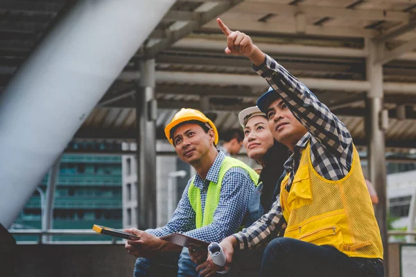 Civil engineer teams meeting working together wear worker helmets hardhat on construction site in modern city. Foreman industry project manager engineer teamwork. Asian industry professional team