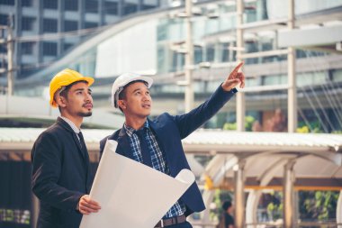 İnşaat mühendisi takımları modern kentteki inşaat sahasında birlikte çalışan işçi kaskı takıyorlar. Foreman Endüstri Mühendislik Mühendisliği ekip çalışması. Asya endüstrisi profesyonel takımı