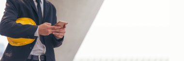 Banner İnşaat mühendisi elinde akıllı telefon tutan sarı bir şapka tutuyor. Panorama Güvenlik miğferi telefon inşaat alanını kullanarak sarı başlık takıyor. Fotokopi alanı olan Banner Hardhat İnşaat