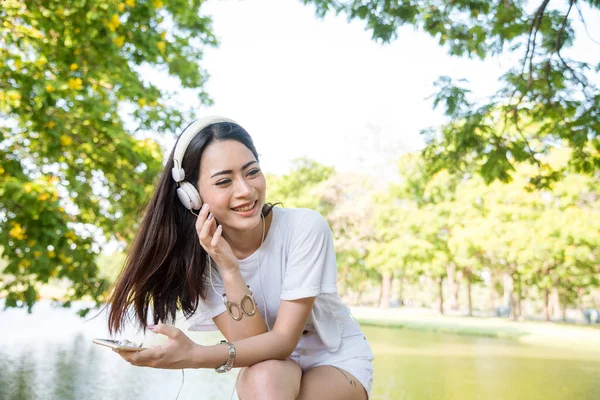 Leisure cheerful wellness woman Concept. Happy teenage woman listening to music wear headphones from smartphone outdoor in the park. Music mental therapist for wellness woman.
