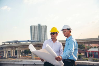 İnşaat mühendisi takımları el sıkışırken inşaat alanında kask takıyor. Foreman Endüstri Projesi Mühendis ekip çalışması. İki Asyalı mühendis takımı el sıkışıyor.