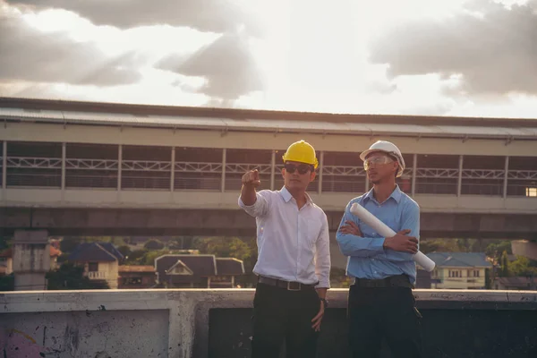 Civil engineer teams meeting working together wear worker helmets hardhat on construction site in modern city. Foreman industry project manager engineer teamwork. Asian industry professional team