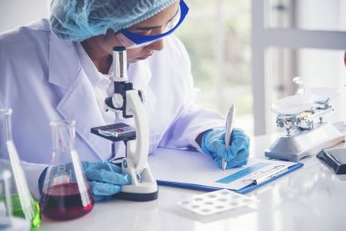 Tıp laboratuarındaki kadın bilim adamı el yazısı bilgileri mikroskop tıbbi testleri, biyoloji kimyasını inceler. Asya kadın teknisyen laboratuarı kan testi farmasötik analizi yapıyor.