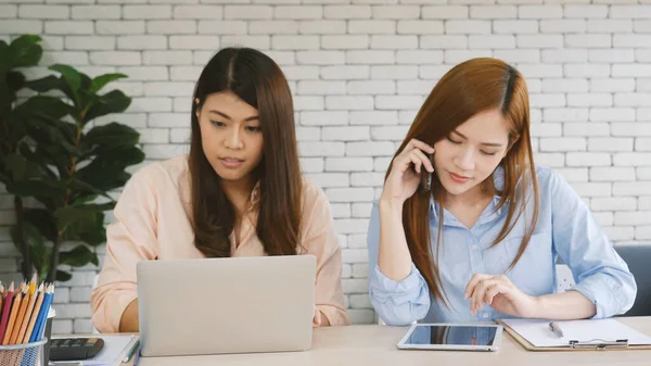 Two businesswomen team meeting using laptop at company office desk. Two young Female freelance reading financial graph charts Planning analyzing marketing data. Asian people team working office firm.