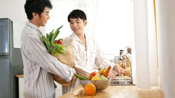 Happy Asian gay couple homosexual cooking together in kitchen prepare fresh vegetable make organic salad healthy food. Asian people happy time smile, laugh in kitchen. Best friend LGBTQ lifestyle