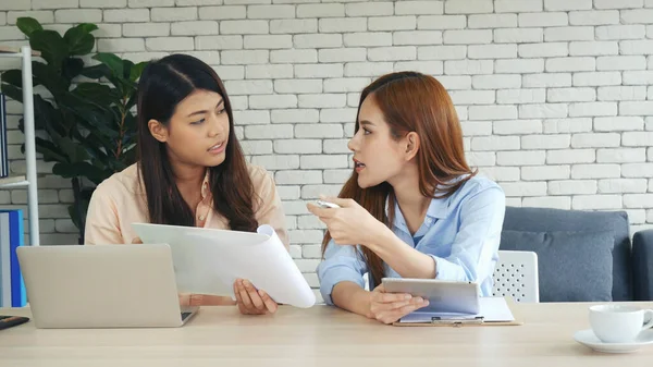 Two businesswomen team meeting using laptop at company office desk. Two young Female freelance reading financial graph charts Planning analyzing marketing data. Asian people team working office firm.