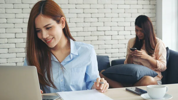 Two businesswomen team meeting using laptop at company office desk. Two young Female freelance reading financial graph charts Planning analyzing marketing data. Asian people team working office firm.