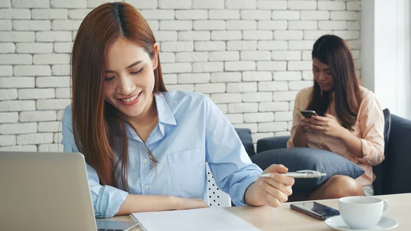 Two businesswomen team meeting using laptop at company office desk. Two young Female freelance reading financial graph charts Planning analyzing marketing data. Asian people team working office firm.