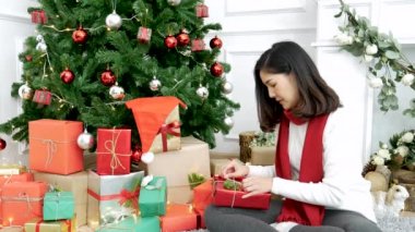 Noel ağacının altında hediye paketi yapan bir kadın. Asyalı kadın dekorasyon balosu balosu Noel ağacı, Noel bayramı kış mevsimsel kutlaması. Hediye paketini sıcak oturma odasına sarın.