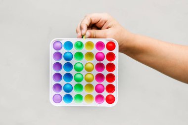 Çocuğun elinde yeni moda bir oyuncak var. Gri arka planda. Pop-it hareketli oyun stresi azaltmaya yardımcı olur.