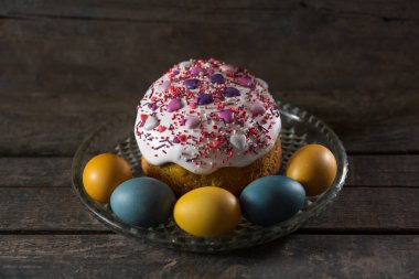 Şeffaf bir tabakta Paskalya pastası, ön planda Ukrayna bayrağının renklerine boyanmış yumurtalar vardır. Sarı ve mavi (cyan). Ahşap dokusunda. Kavram: yiyecek, tatil, Ukrayna 'da savaş