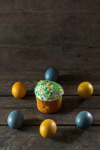 Painted eggs for Easter in the colors of the flag of Ukraine and Easter cake. Yellow and blue (cyan). On wood texture. Concept: food, holiday, war in Ukraine