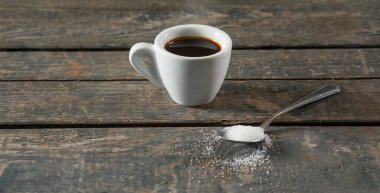 Hot black coffee or espresso in a white ceramic cup on a wooden texture background. Next to a spoonful of sugar