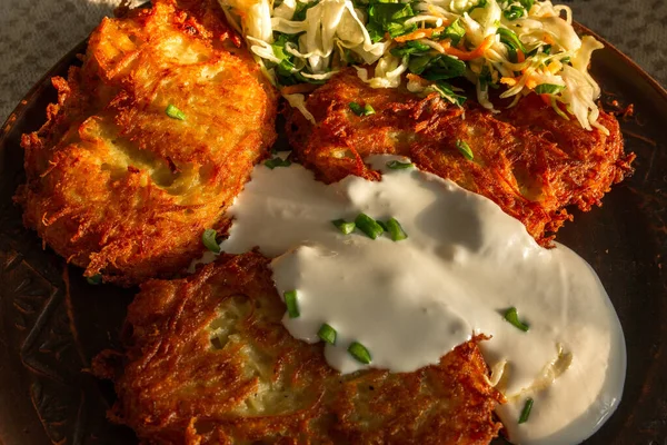 Keten kahverengi tabakta kızarmış patates gözlemesi, ekşi krema, yeşil soğan, lahana salatası ve havuç. Yemek, patates gözlemesi, yemek.