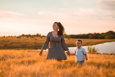 Mom kisses her son on the head in a wheat field at sunset