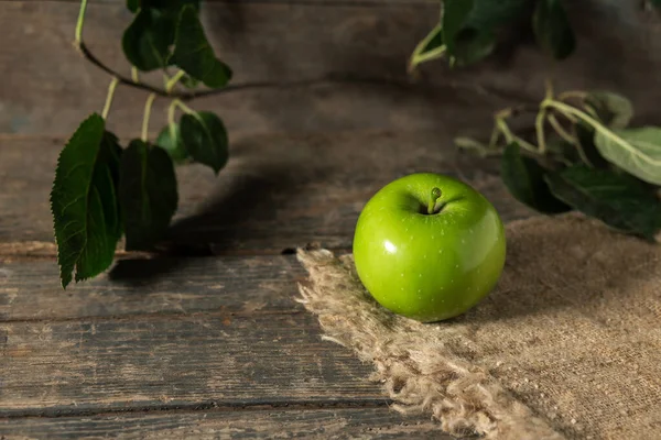 Green apple with leaves on burlap on wooden boards