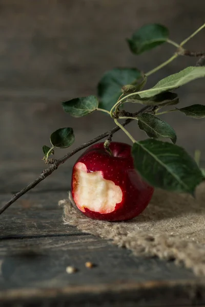 a bitten red apple with leaves on burlap on wooden planks