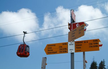 Signs for various mountain hiking trails in Switzerland with gondola in the background