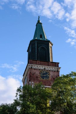 Turku Katedrali, Finlandiya 'da ortaçağ bazilikası yazın mavi gökyüzüne karşı ön planda ağaçlarla birlikte.