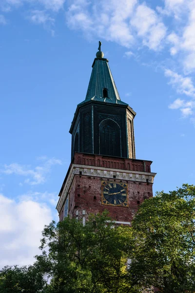 Turku Katedrali, Finlandiya 'da ortaçağ bazilikası yazın mavi gökyüzüne karşı ön planda ağaçlarla birlikte.