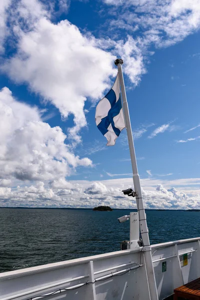 Finlandiya 'nın Turku Takımadası' ndaki bir geminin arka planında bulutlu ve adalı bir Finlandiya bayrağı dalgalanmaktadır..