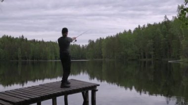 Yazın Finlandiya 'da bir göldeki ahşap iskelede balık tutan adam.