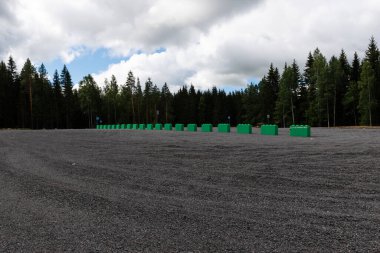 Arka planda kozalaklı bir orman olan boş çakıl taşı otoparkı.