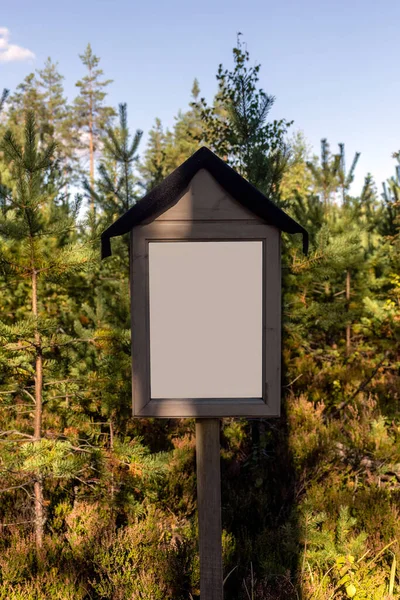 Empty white sign in nature, with green trees in the background