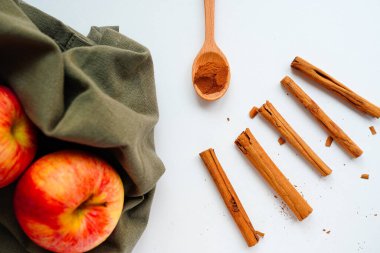 Tarçın çubukları ve tarçın tozu, beyaz bir masada kırmızı elmalar