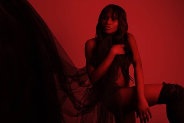 Uzun saçlı ve kırmızı arka planda poz veren çekici siyahi bir kadın..