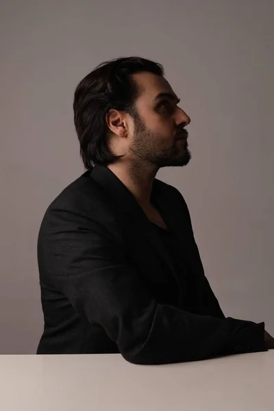 Vista lateral del hombre barbudo en traje negro sentado sobre fondo blanco. Vertical. — Foto de Stock