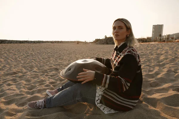 Mulher toca música relaxante com handpan tambor pendurar enquanto sentado na praia. — Fotografia de Stock