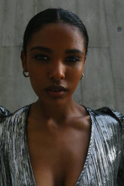 Gri duvarda poz veren Afrikalı Amerikalı genç bir kadının portresi. Dikey.