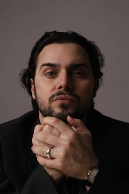 Beyaz duvarın üzerinde oturan şık sakallı adam kameraya bakıyor. İzole edilmiş.