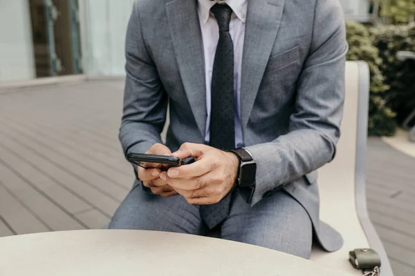 Gehakte foto van zakenman met behulp van zijn smartphone, zitten buiten. — Stockfoto