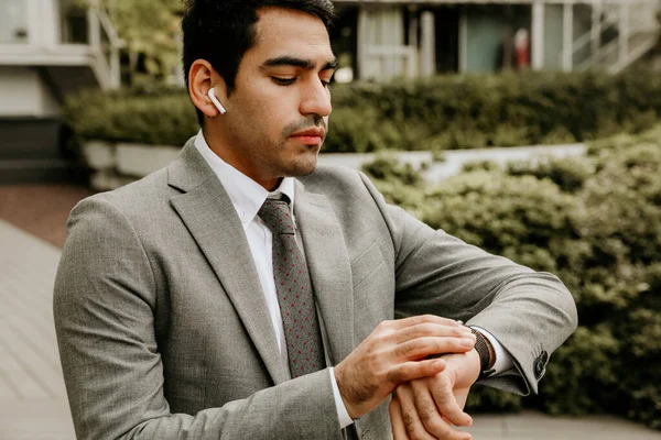 Joven hombre de negocios buscando elegante mirando su reloj inteligente, posando al aire libre. — Foto de Stock