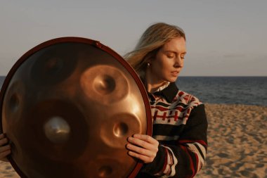 Kadınlar plajda otururken davul sapını tutarlar. Meditasyon havası.