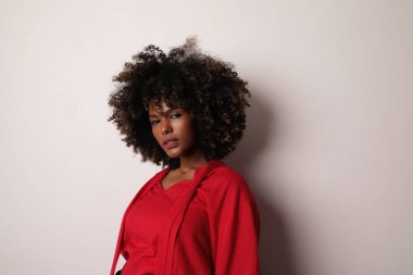 Beyaz arka planda kırmızı bluz giyen kıvırcık saçlı Afro-Amerikalı kadın..