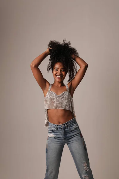 Retrato de bela jovem negra na parede cinza, tocando seu cabelo encaracolado. — Fotografia de Stock