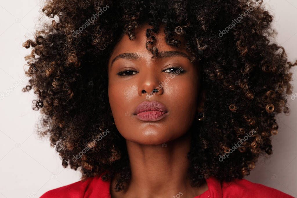 Headshot of African American young woman with curly hair over white background.