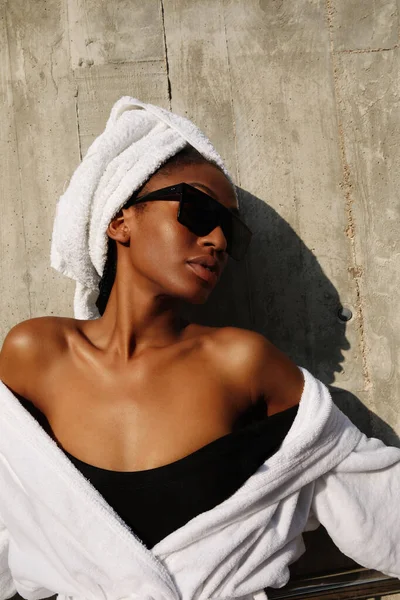 Beyaz havluya sarılı gri duvarda poz veren genç bir kadının vesikalığı. Dikey.